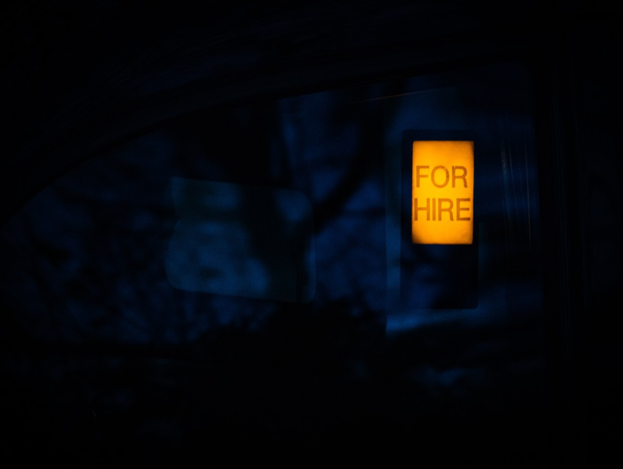 Imagen de cartel luminoso naranja con texto "FOR HIRE" sobre un fondo abstracto muy oscuro