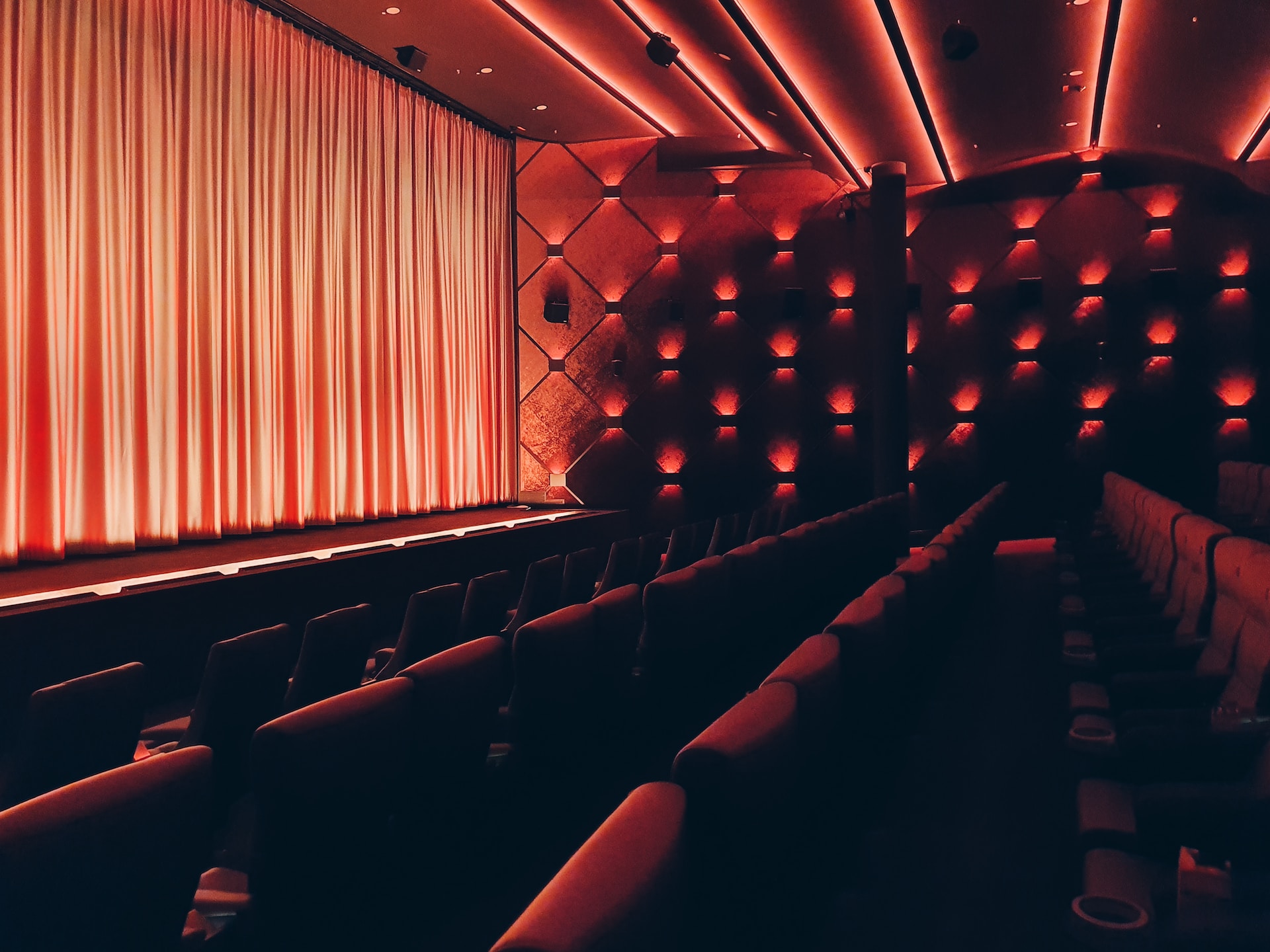 Sala de cine roja, vacía, vista lateral a asientos, escenario y telón