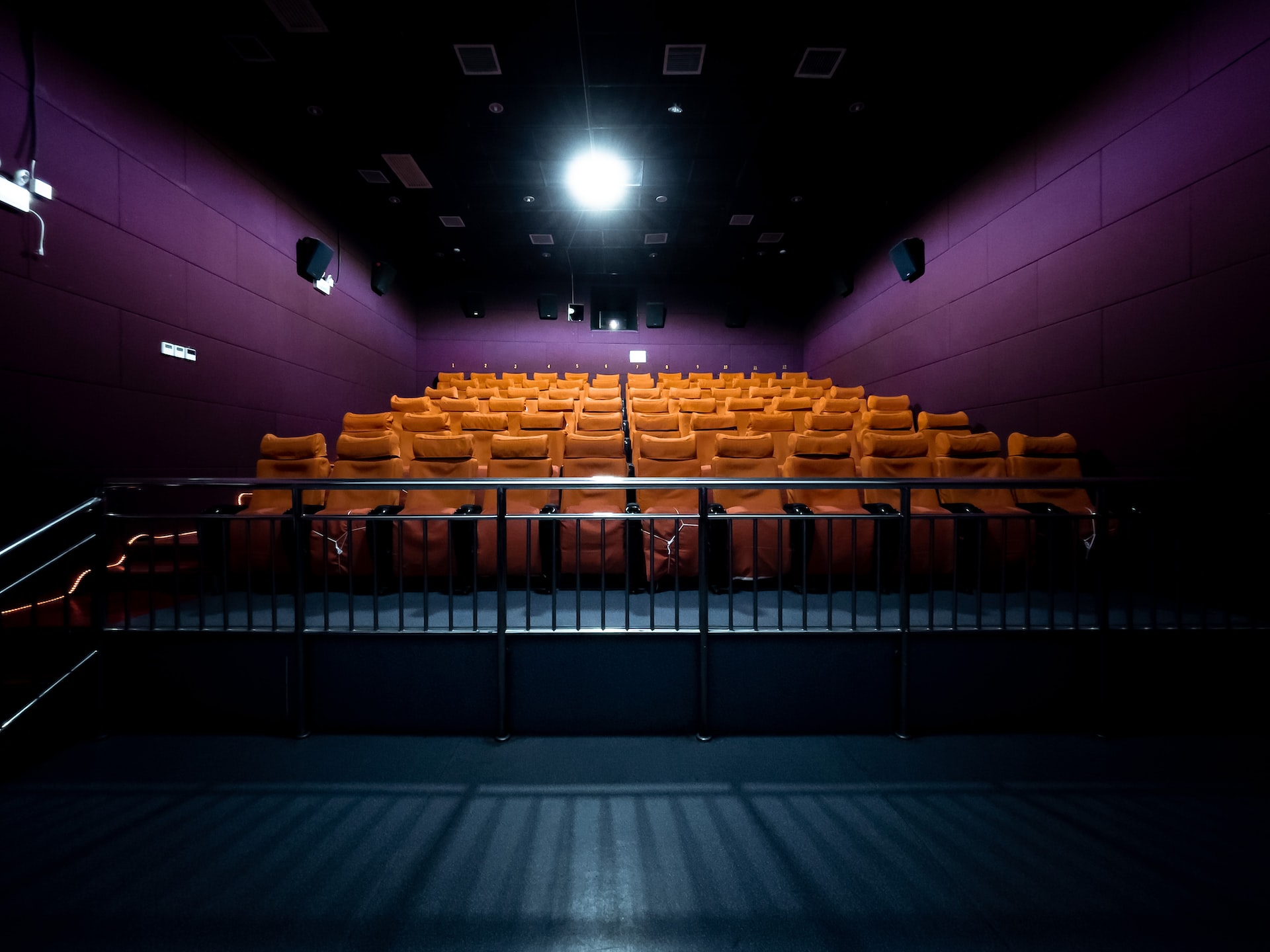 Sala de cine vacía con asientos amarillos, paredes moradas y suelo azul