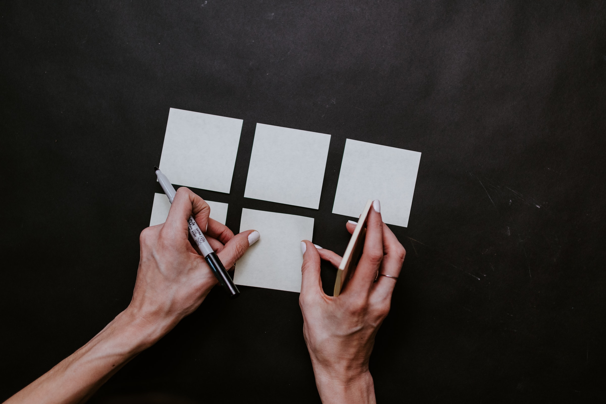 Dos manos de mujer colocando post-it sobre una superficie negra, vistas desde arriba