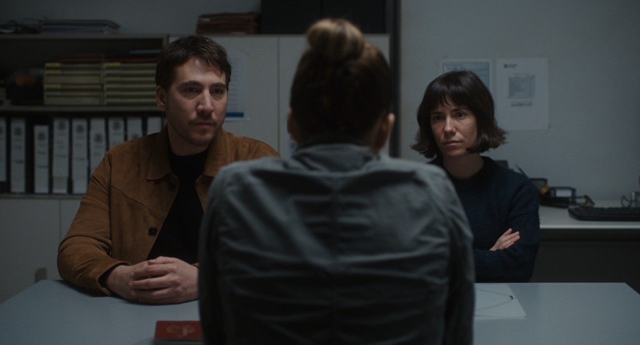 Dos personas mirando de frente a un policía que les interroga